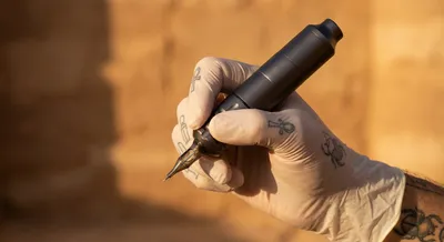 Main d'un tatoueur tenant une machine rotative moderne en Égypte.